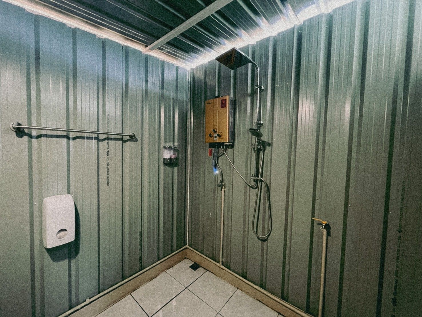 A small, enclosed shower area with a handheld showerhead, a soap dispenser, and a towel rack.