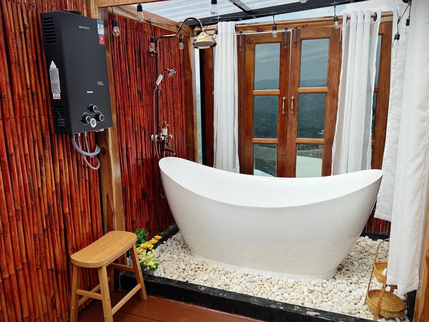 A bathroom with a freestanding bathtub, wooden wall paneling, a shower with a rain showerhead, and a window with curtains.