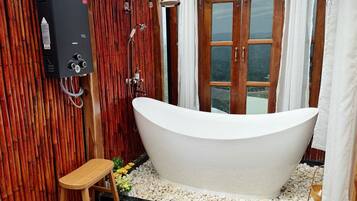A bathroom with a freestanding bathtub, wooden wall paneling, a shower with a rain showerhead, and a window with curtains.
