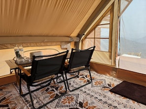 A tented room with a table, two chairs, a patterned floor, and a view through a window.