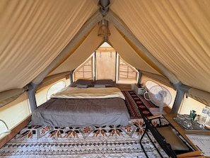 A tent with a bed, a fan, and a table with items.