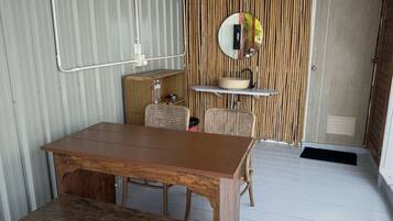 A compact room with a wooden table and bench, a small cabinet, wicker chairs, a bamboo partition, and a mirror on the wall.