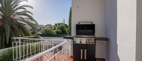 An outdoor grill area with a white wall and a metal railing.