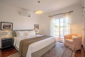 A bedroom with a large bed, a nightstand, a chair, and a window with curtains. - Luxurious Villa | Pool, Hot Tub, Cinema and Golf (Quarteira)