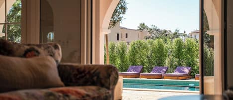 A room with a view of a swimming pool and lounge chairs outside.
