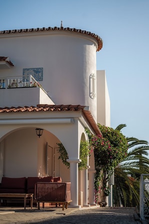 A building with a curved facade, a balcony with a railing, and a seating area with a bench and a table. - Luxurious Villa | Pool, Hot Tub, Cinema and Golf (Quarteira)