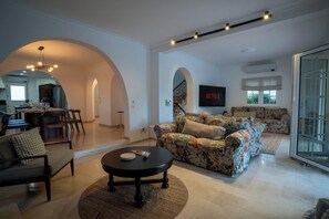 A spacious living area with a sofa, armchairs, a coffee table, and a flat-screen TV mounted on the wall. - Luxurious Villa | Pool, Hot Tub, Cinema and Golf (Quarteira)