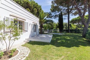 A white building with a paved entrance, surrounded by a well-maintained lawn and trees. - Portuguese mansion close to marina, golf and beach (Quarteira)