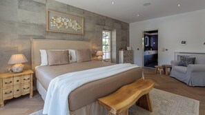 Ein Schlafzimmer mit einem großen Bett, Nachttischen, einer Bank, einem Sofa und Blick auf die Küche.