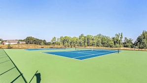 Un court de tennis avec un filet, entouré d’arbres et sous un ciel dégagé.