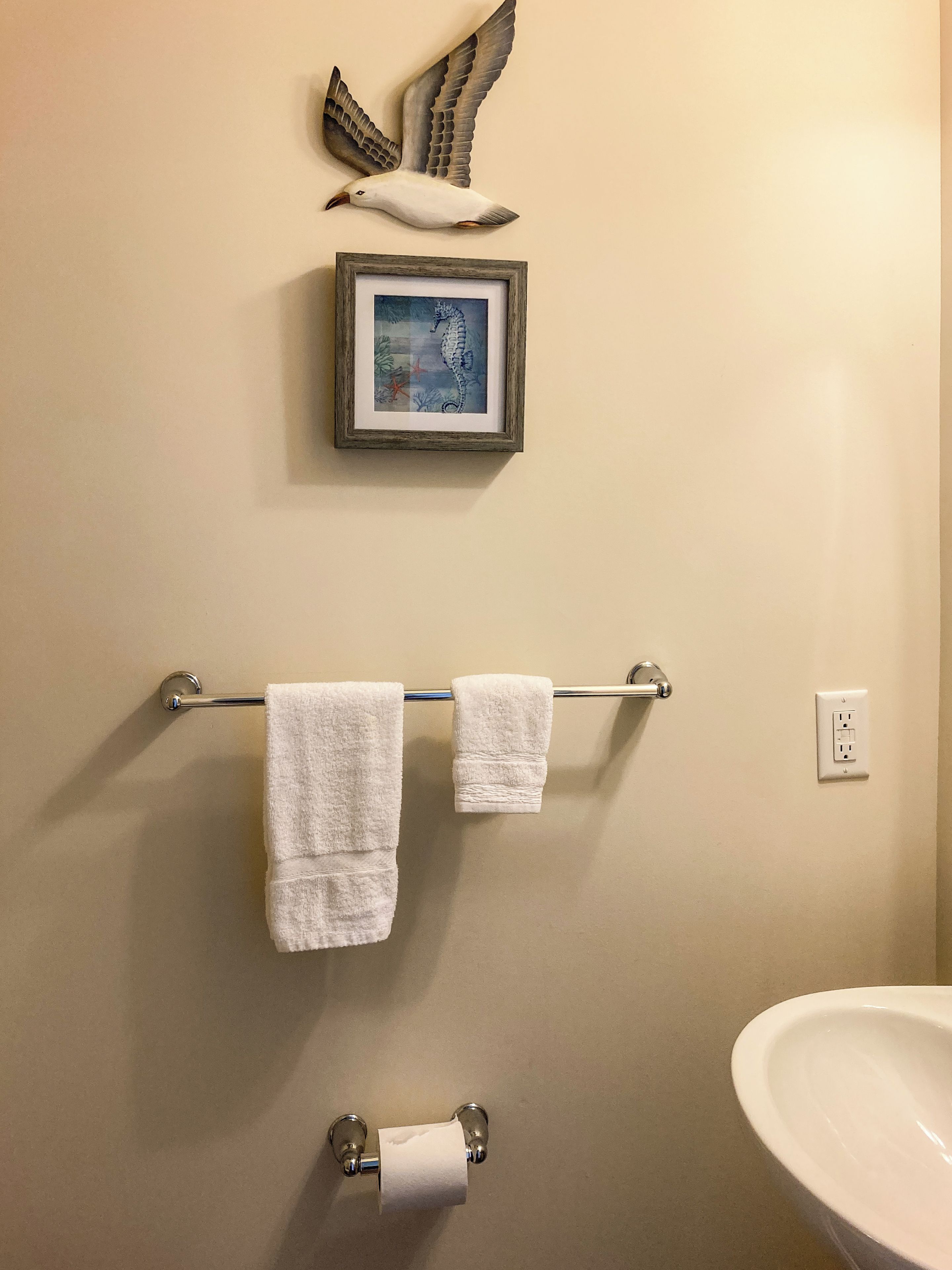 A bathroom with a towel rack, a framed picture, a toilet paper holder, and a sink.
