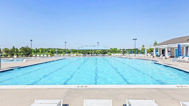 Une grande piscine extérieure avec plusieurs couloirs de nage, entourée de chaises longues et de parasols, et une zone abritée en arrière-plan.