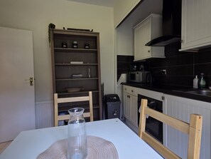 Une cuisine avec des meubles blancs, un four à micro-ondes et un plan de travail noir.