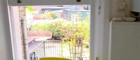 Una habitación con ventana que da a un jardín, una mesa blanca y una silla amarilla.