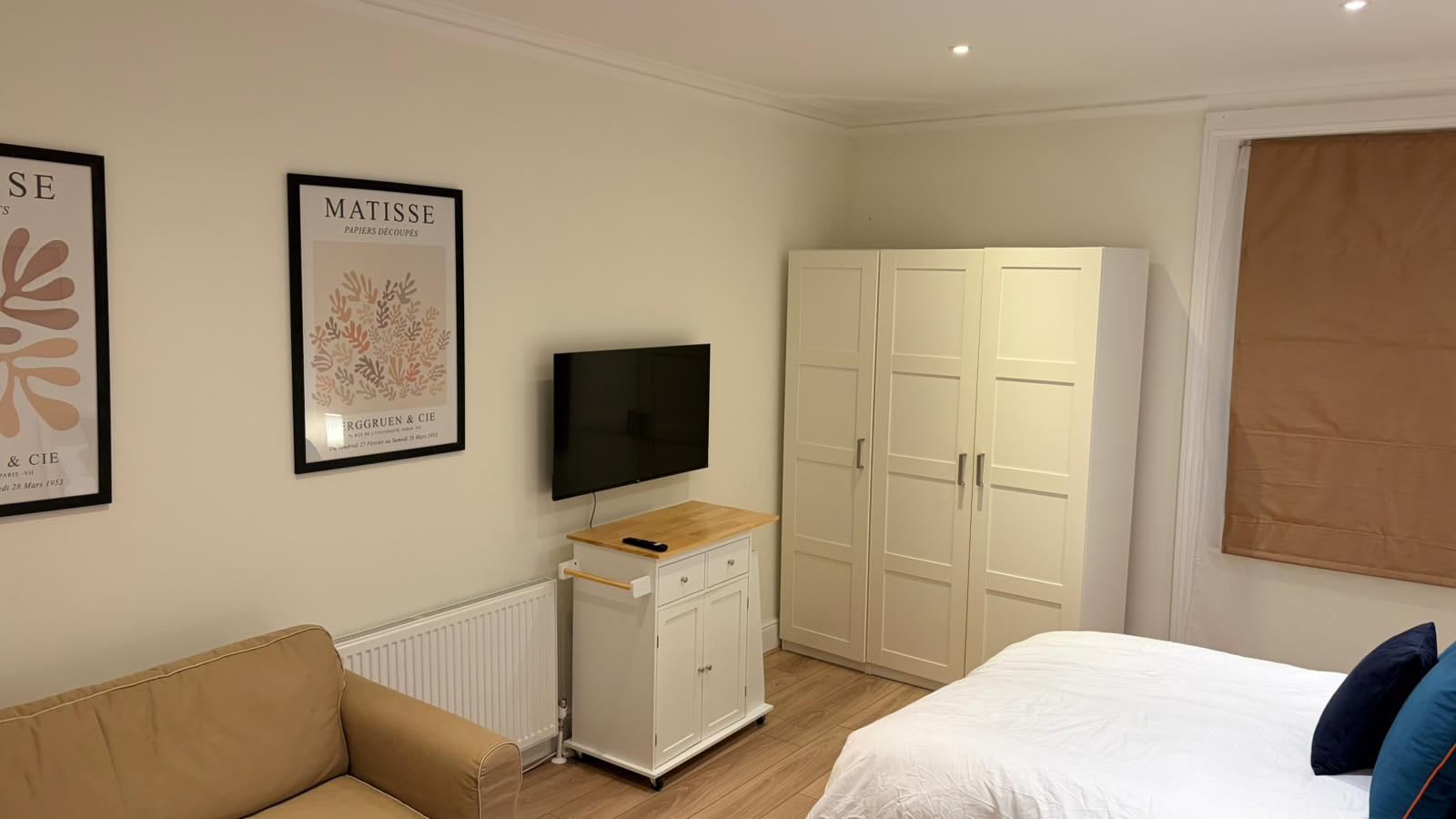 Une chambre à coucher avec un lit, une télévision, une armoire et deux tableaux encadrés accrochés au mur.