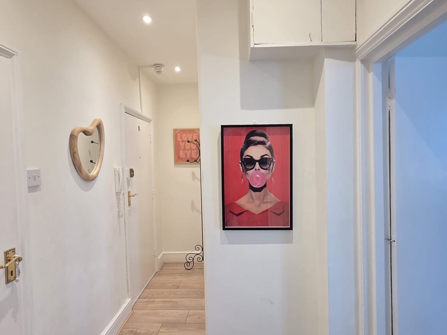 A hallway with a wooden door, a framed mirror, a red framed artwork, and a light switch on the wall.
