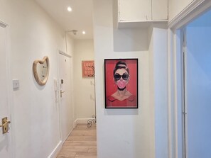Un couloir avec une porte en bois, un miroir encadré, une œuvre d’art encadrée de couleur rouge et un interrupteur sur le mur.