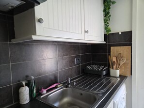 A kitchen with a stainless steel sink, a dish rack, and a set of wooden utensils. - Spacious South Kensington apartment near museums (South Kensington)