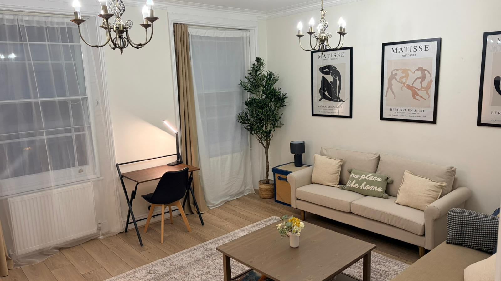 Una sala de estar con un sofá, una mesa de centro, un escritorio con una silla y dos obras de arte enmarcadas en la pared.