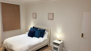 A bedroom with a bed, pillows, a bedside table with a lamp, and a door. - Spacious South Kensington apartment near museums (South Kensington)