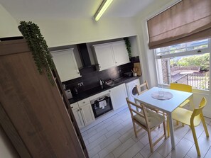 A compact kitchen with white cabinets, a black countertop, and a dining area with yellow chairs. - Spacious South Kensington apartment near museums (South Kensington)