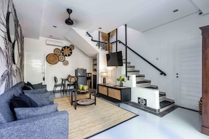 A modern living room with a sofa, a dining area, and a staircase.