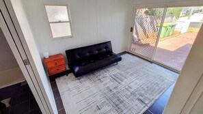 A room with a black sofa, a wooden nightstand, and a patterned rug.