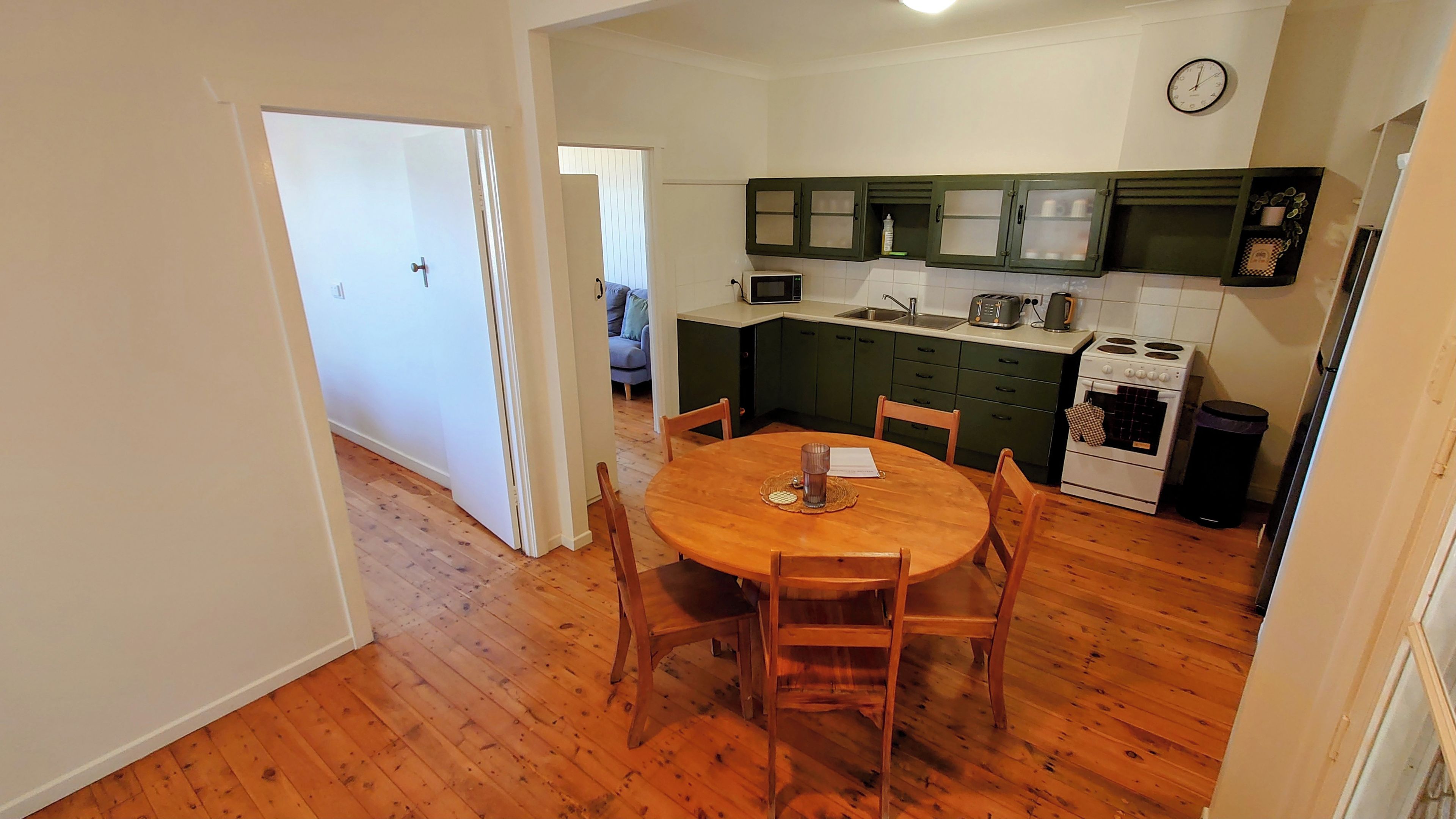 A compact kitchen with a dining table, wooden chairs, a microwave, a stove, and cabinets.