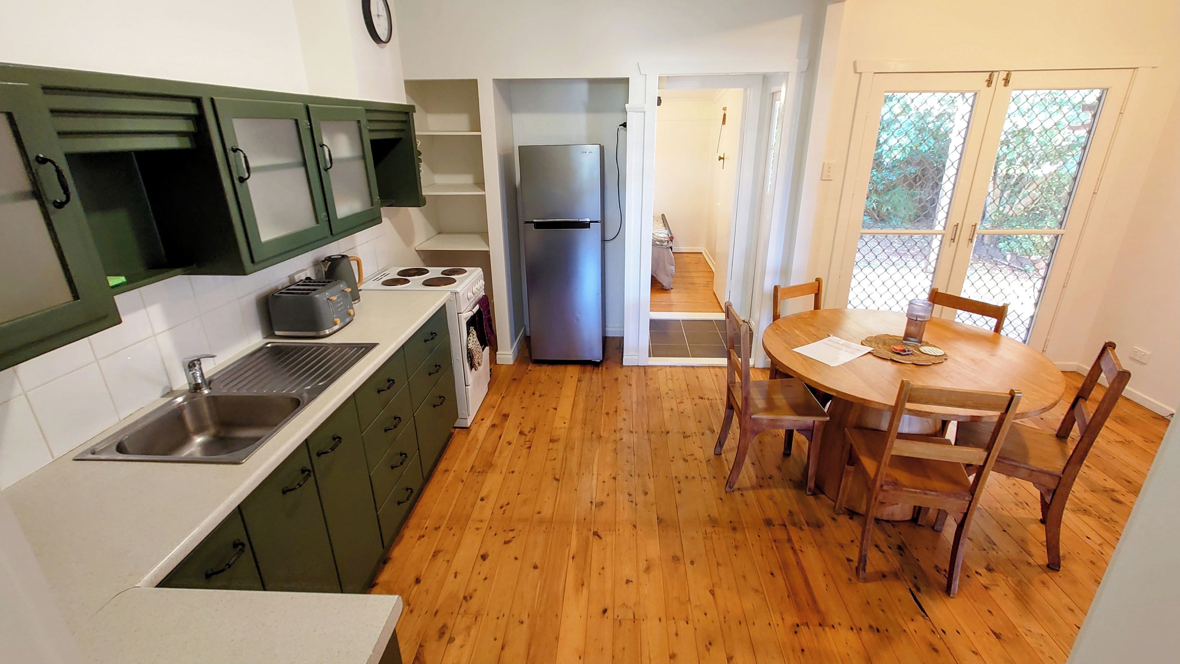 A compact kitchen with a sink, stove, and refrigerator, leading to a dining area with a table and chairs.