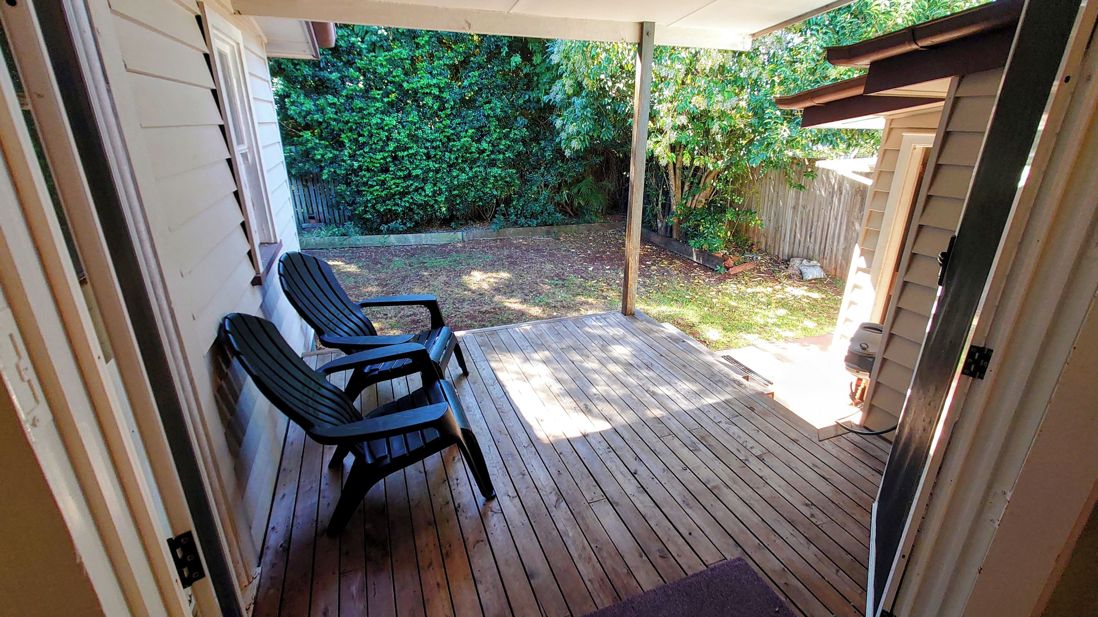 A covered patio with wooden flooring and two chairs.