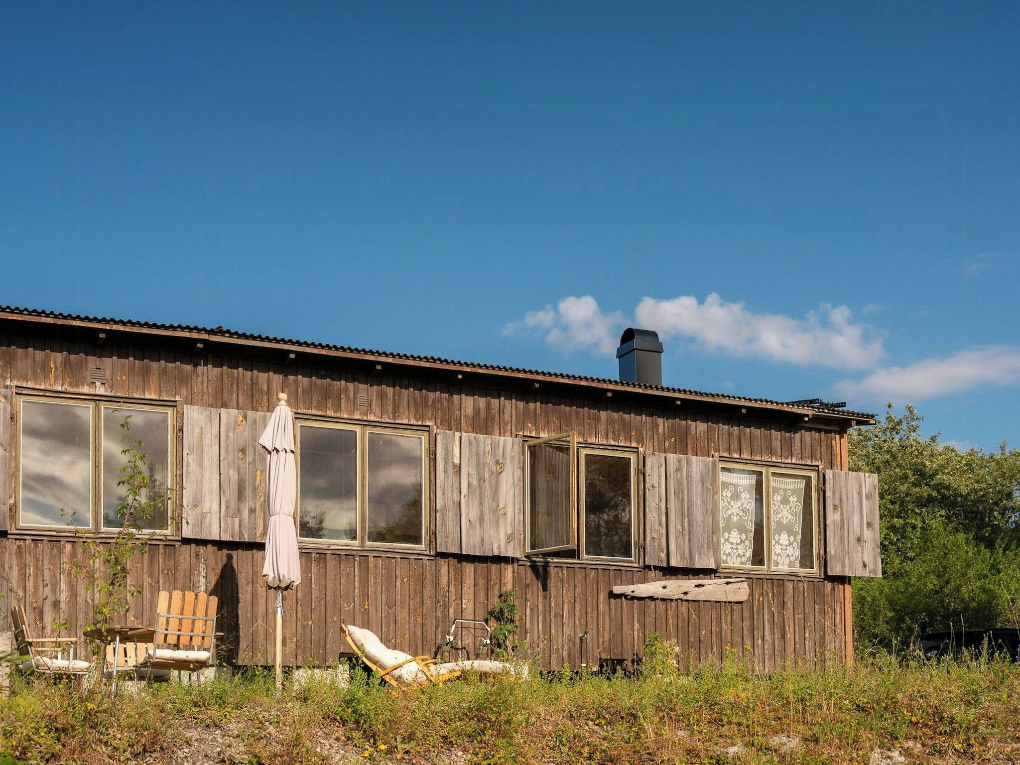 A dilapidated wooden building with boarded-up windows, a chimney, and outdoor furniture.
