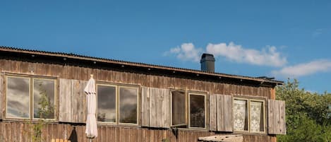 A dilapidated wooden building with boarded-up windows, a chimney, and outdoor furniture.