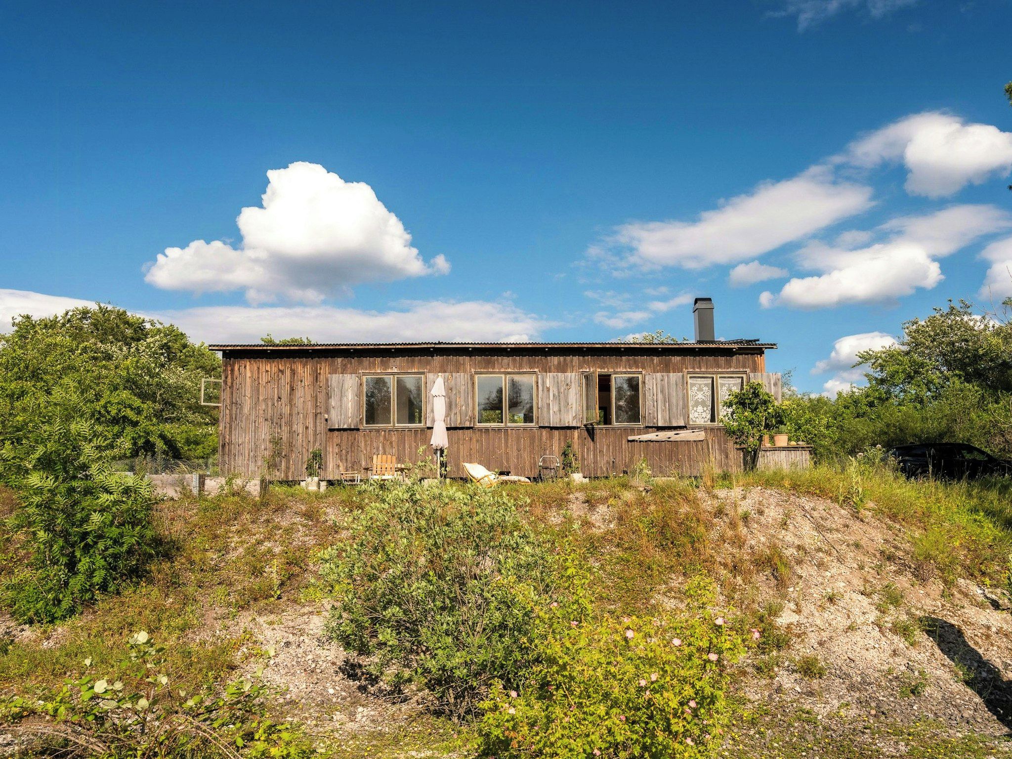 Ein rustikales Holzhaus mit Schornstein, umgeben von üppiger Vegetation und blauem Himmel.