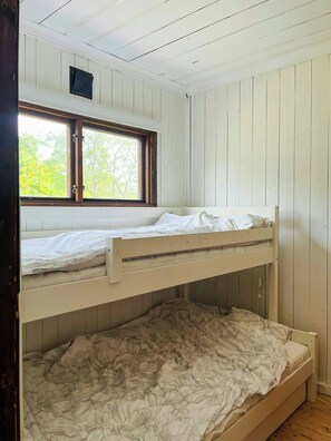 Ein Schlafraum mit Etagenbetten, einem Fenster, Holzwänden und einer weißen Decke.