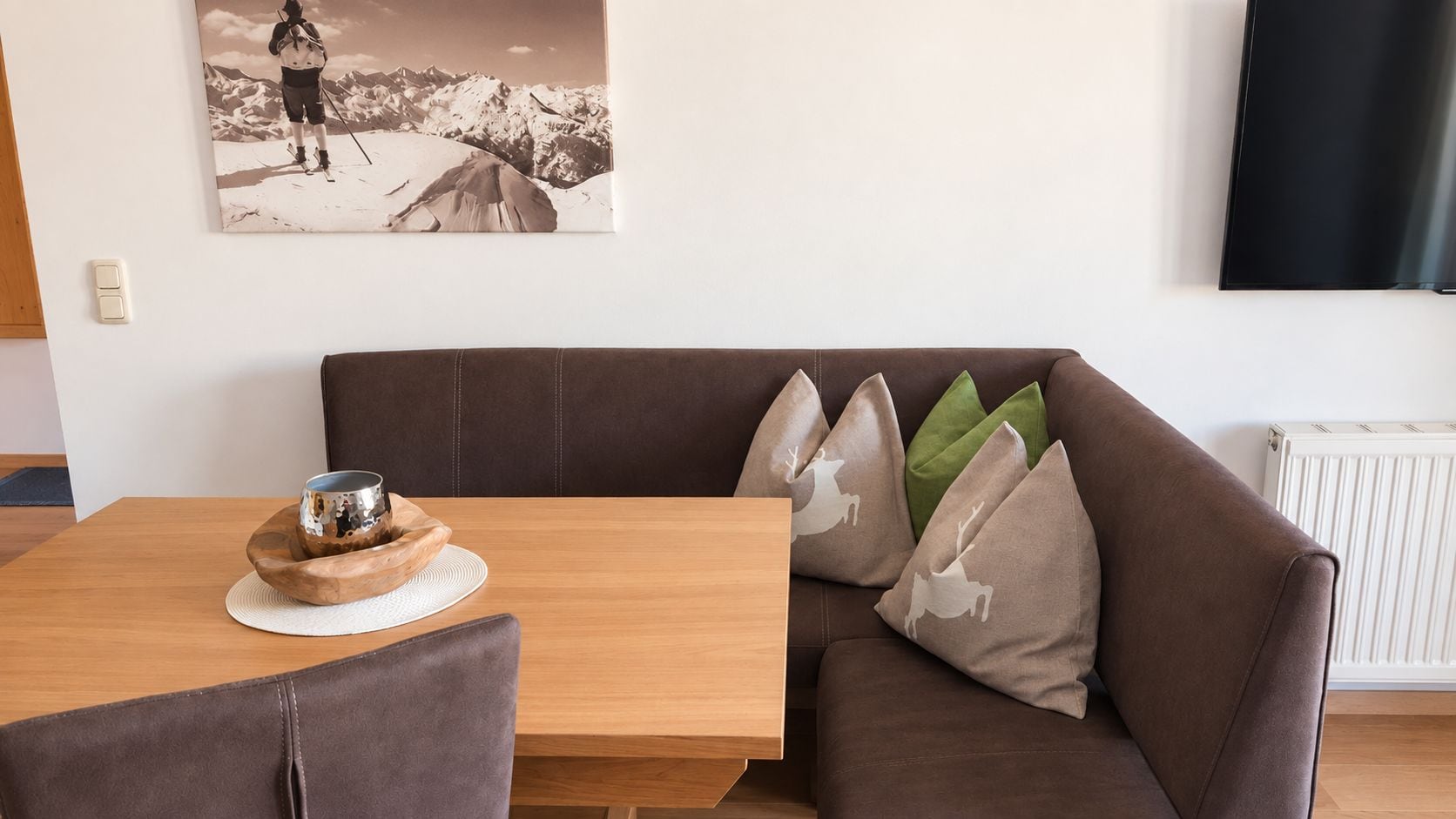 Una sala de estar moderna con un sofá de cuero marrón, una mesa de comedor de madera y un cuadro de un paisaje montañoso en la pared.