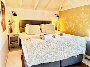 A bedroom with a bed, bedside tables, a nightstand, a lamp, and a wall with a floral pattern.