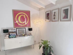 A room with a white cabinet, a large abstract painting, a floor lamp, and a potted plant.