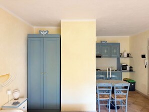 A room with a blue wardrobe, a dining table with chairs, and a kitchen area with cabinets and appliances. - Ginestre Smeraldo by Casa Check (Olbia)