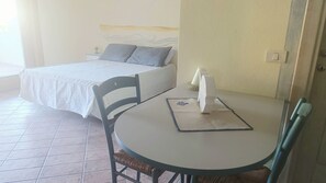 A bedroom with a bed, bedside table, and a small round table with a chair. - Ginestre Smeraldo by Casa Check (Olbia)