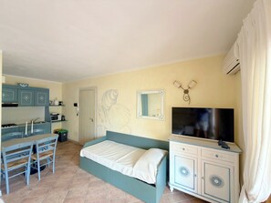 A bedroom with a bed, a TV, a desk with a chair, and a kitchenette. - Ginestre Smeraldo by Casa Check (Olbia)