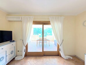 A room with a sliding glass door leading to an outdoor patio, a television on a cabinet, and a tiled floor. - Ginestre Smeraldo by Casa Check (Olbia)