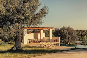 A modern outdoor seating area with a pergola, tables, and chairs, adjacent to a swimming pool. - Trulli between Tradition and Comfort with Pool (Ostuni)