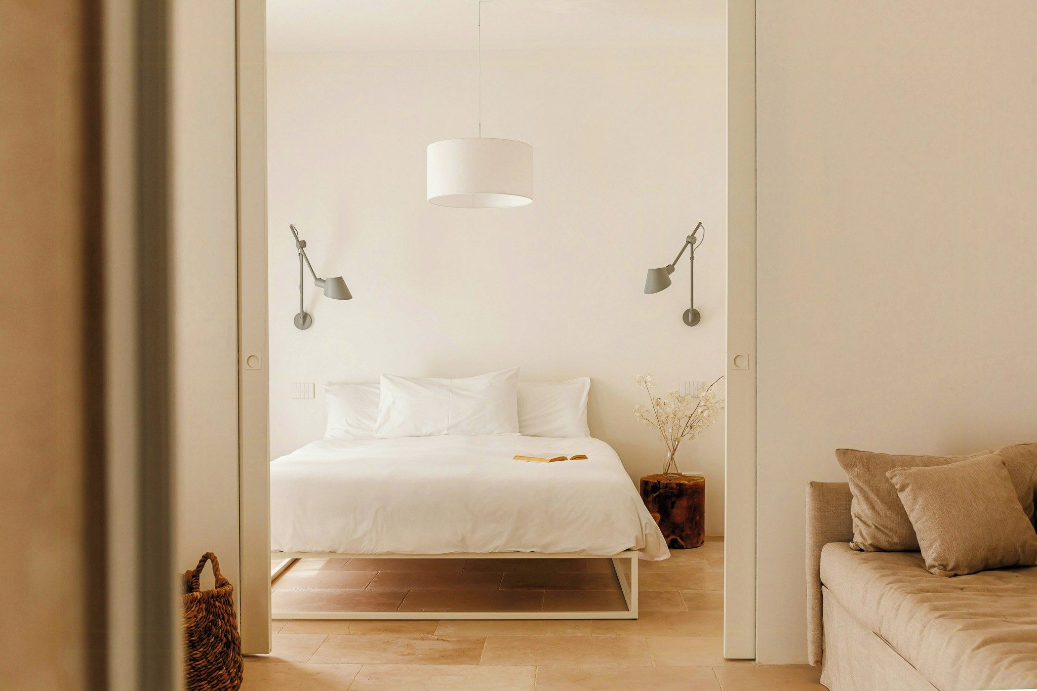 Een slaapkamer met een bed, bedlampen, een nachtkastje met een vaas en een bank.