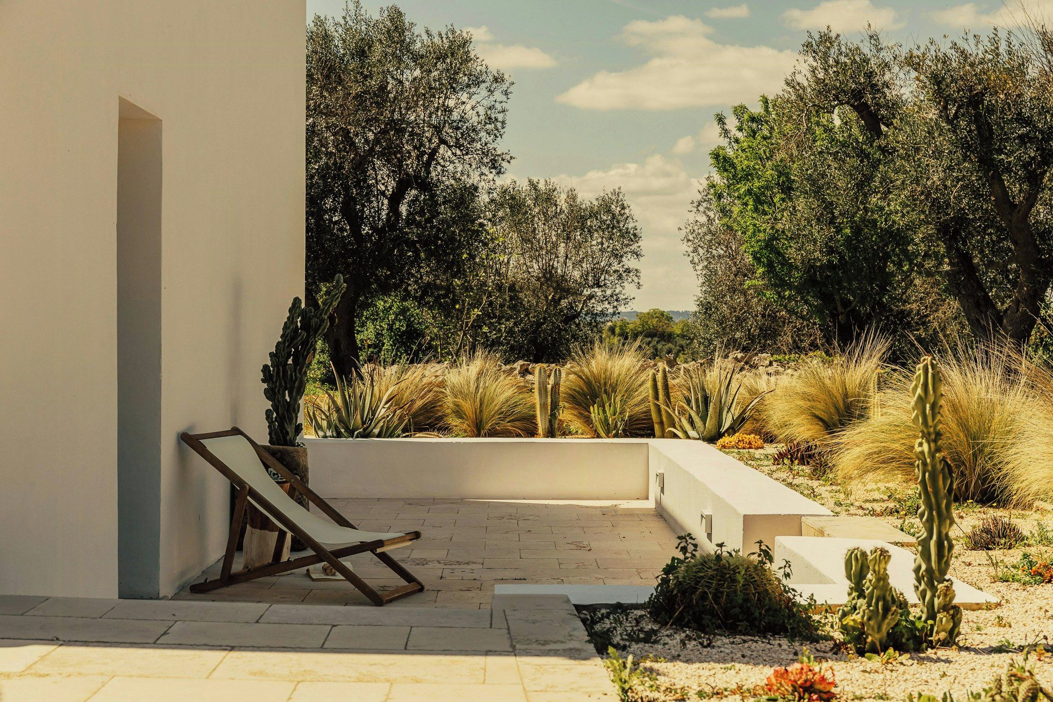 A modern outdoor patio with a lounge chair, cacti, and a variety of shrubs.