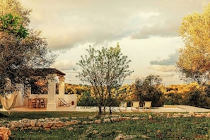 A serene outdoor setting with a white building, a hammock, a dining table with chairs, and a pool area with lounge chairs. - Trulli between Tradition and Comfort with Pool (Ostuni)