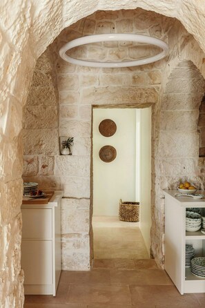 A narrow stone archway leading to a room with a white cabinet, a woven basket, and a bowl of fruit on a table. - Trulli between Tradition and Comfort with Pool (Ostuni)