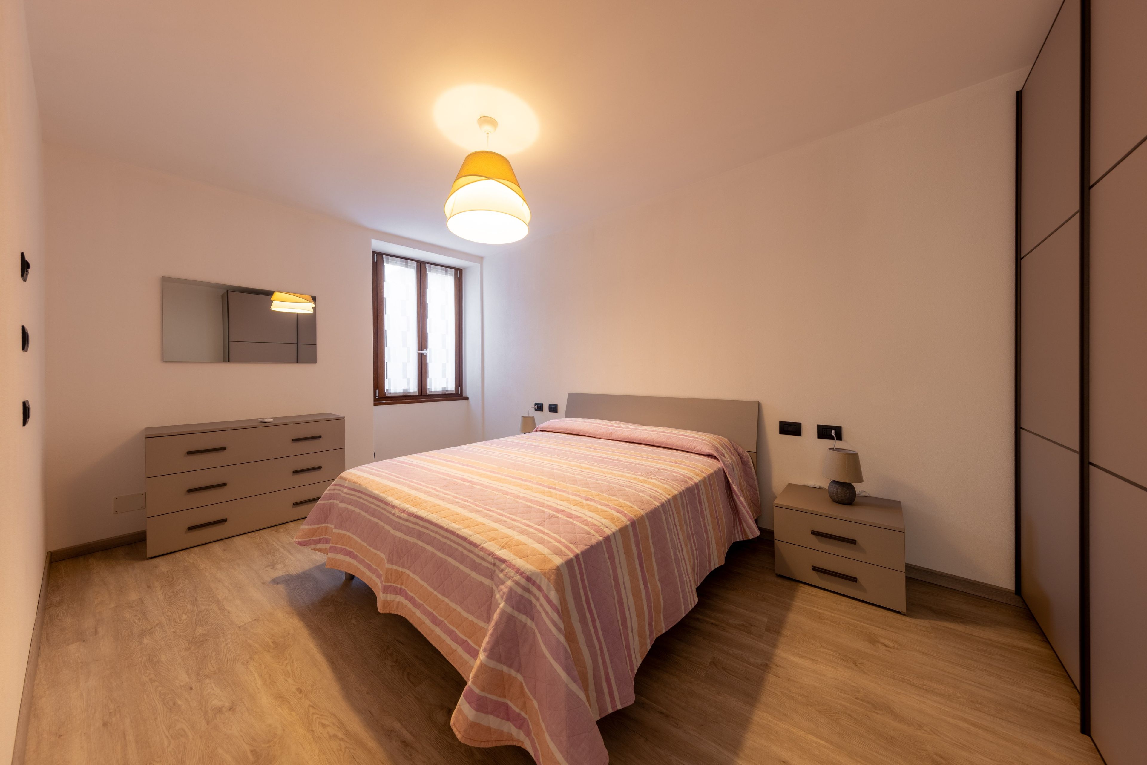 A bedroom with a bed, dresser, bedside tables, and a window.