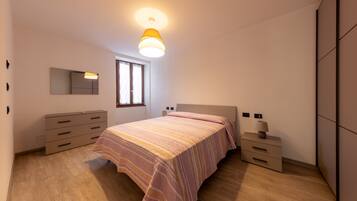 A bedroom with a bed, dresser, bedside tables, and a window.