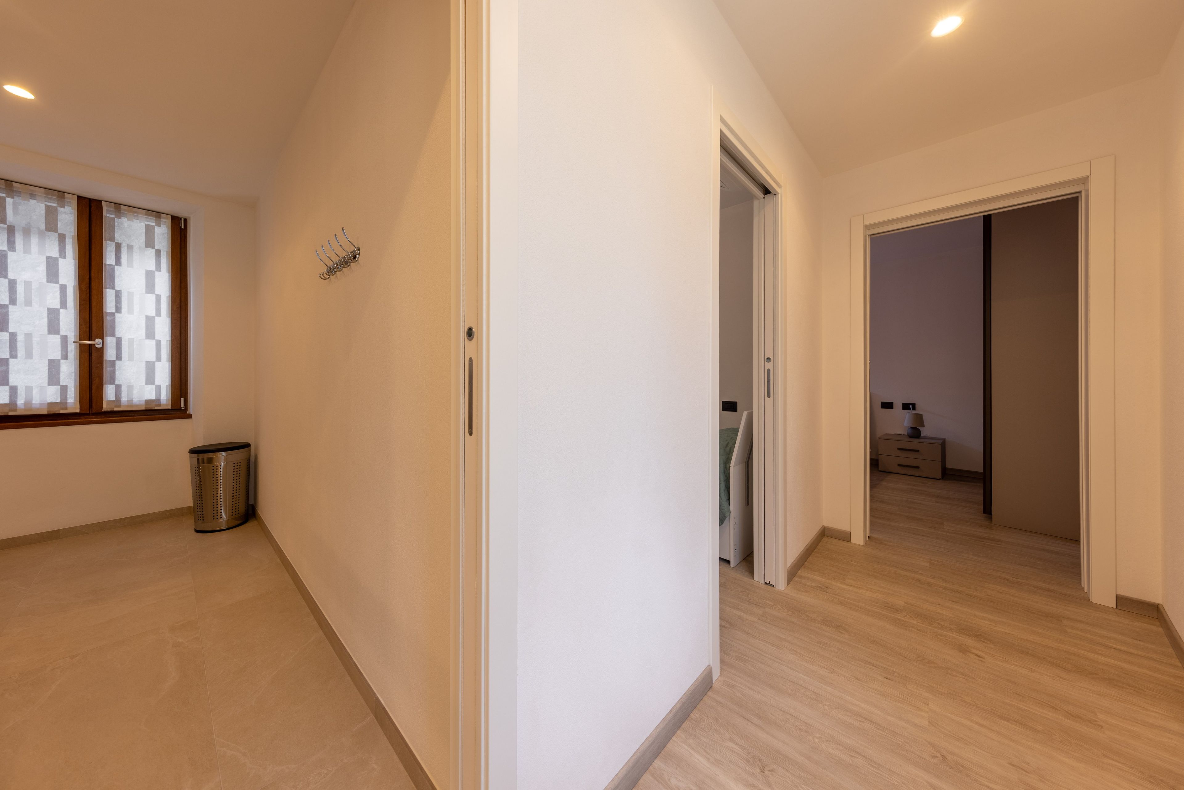 A hallway with a window, a door, and a trash bin.