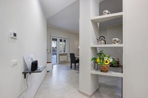 Ein Flur mit weißer Wand, einem Thermostat, einer Steckdose und einem Regal mit Wasserkocher und Tasse.